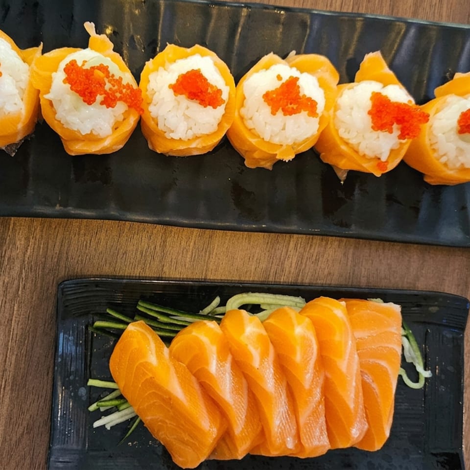 Japanese sushi spread featuring salmon sashimi and orange-wrapped rice rolls topped with bright red roe on black plates.