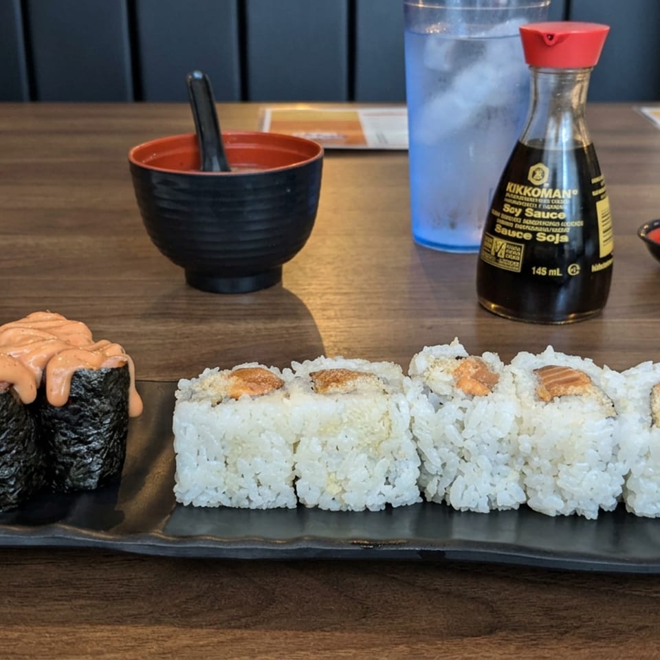 Sushi platter with salmon-topped rolls and seaweed-wrapped pieces, accompanied by soy sauce, pickled ginger, chopsticks, and tea.